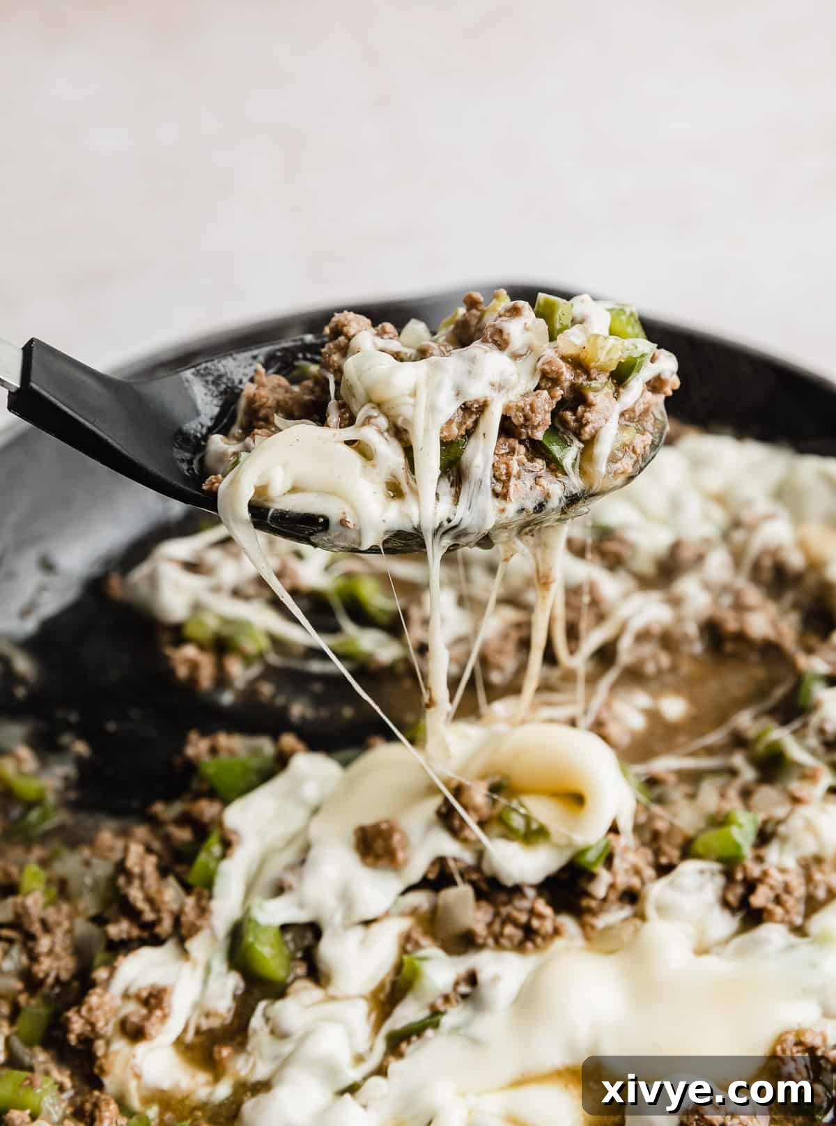 Philly Cheesesteak Joes 8 A large black spoon carefully scooping up a hearty portion of the delicious Philly Cheesesteak Sloppy Joes mixture directly from the skillet, ready for serving.