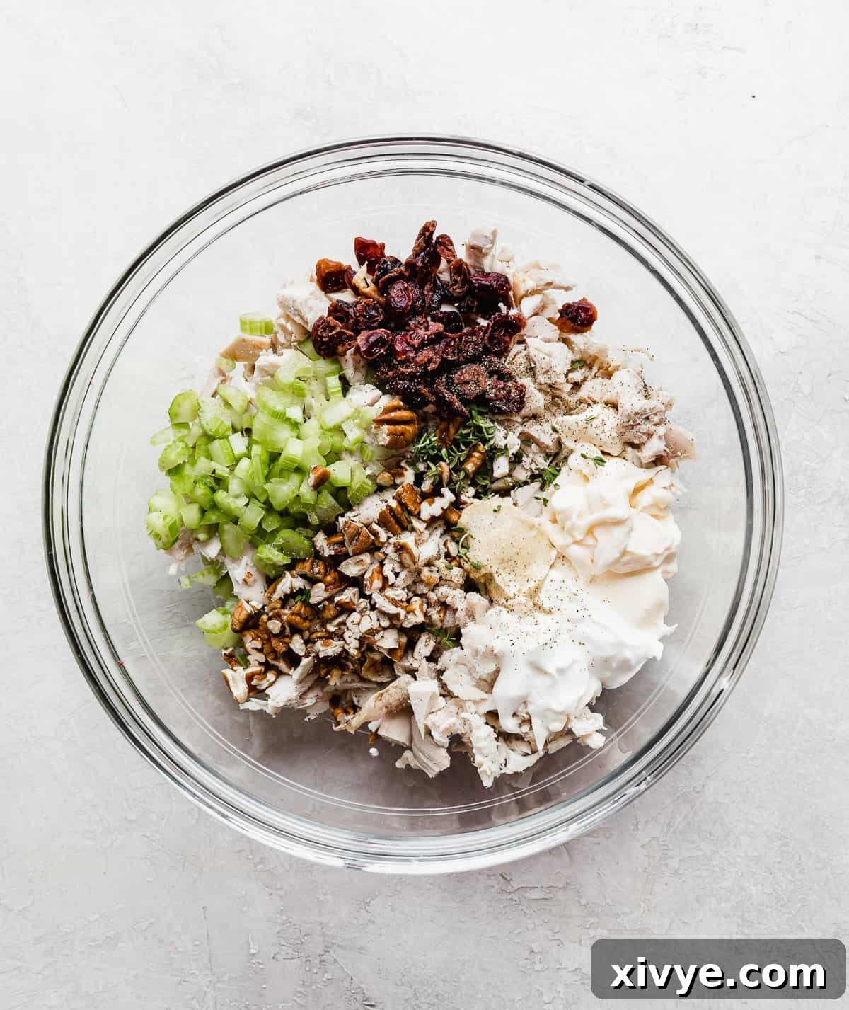 A glass bowl with turkey salad ingredients in it: celery, turkey, dried cranberries, pecans, mayo.