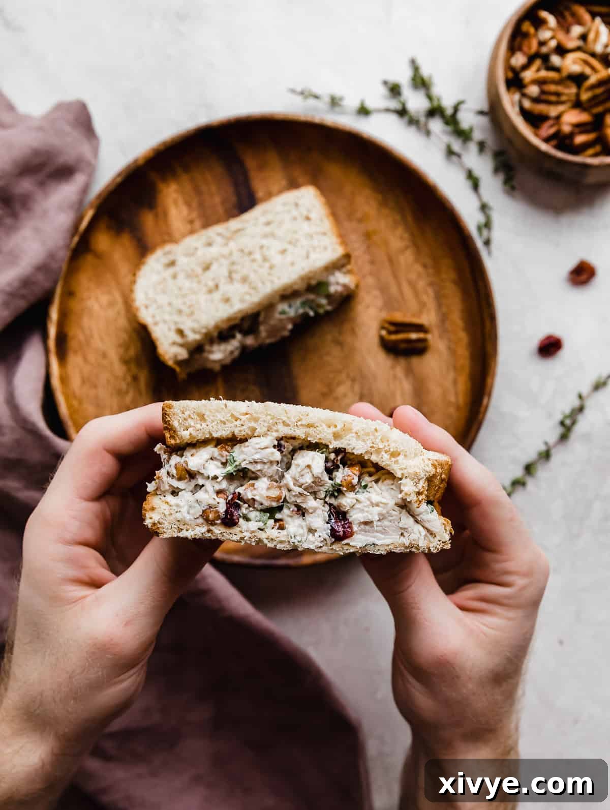 A hand holding a slice of Leftover Cranberry Turkey Salad Sandwich overtop of a gray background.