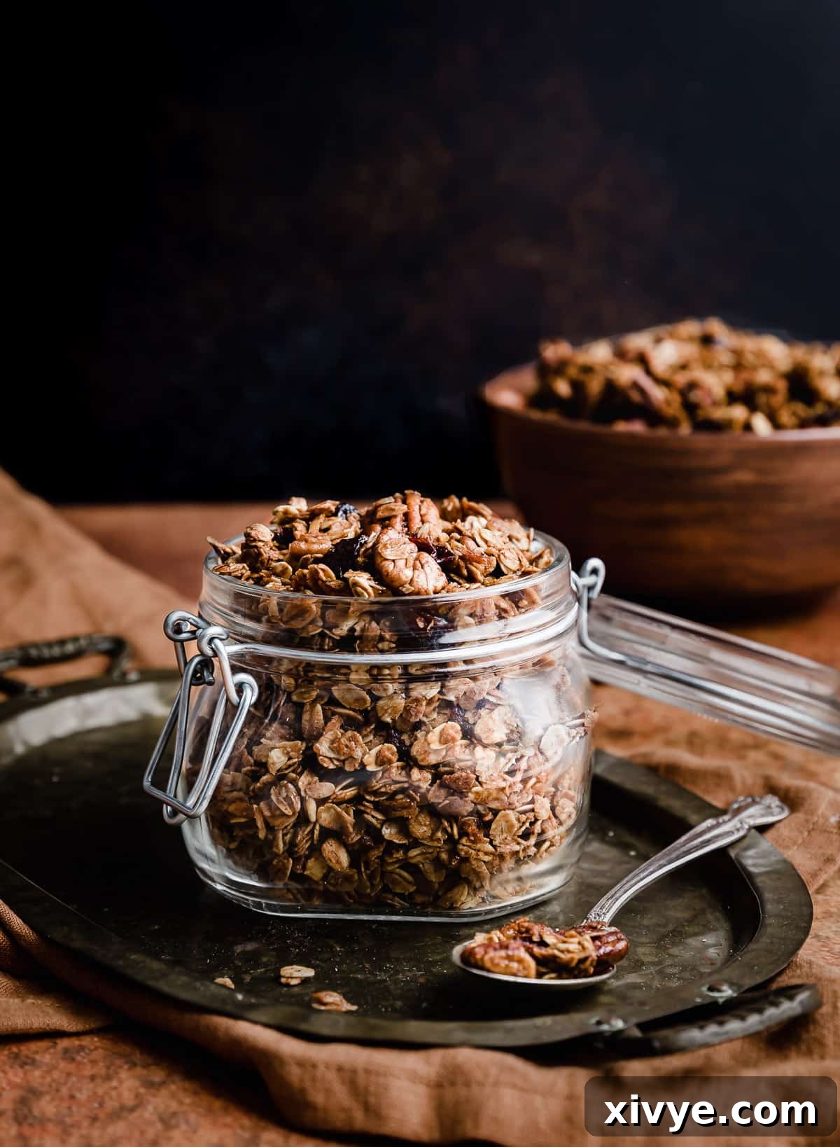 Festive Gingerbread Granola 2 Homemade Gingerbread Granola in a clear glass jar, set against a dark brown, inviting background.