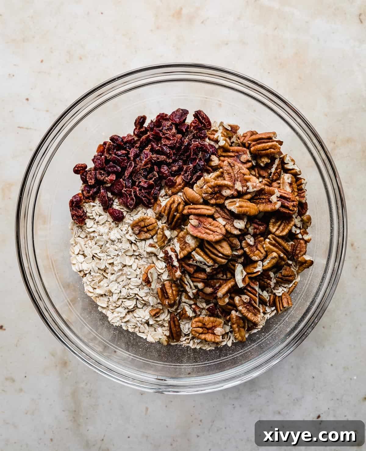 Festive Gingerbread Granola 4 A glass bowl containing a mix of rolled oats, pecans, and dried cranberries, ready for the wet ingredients.