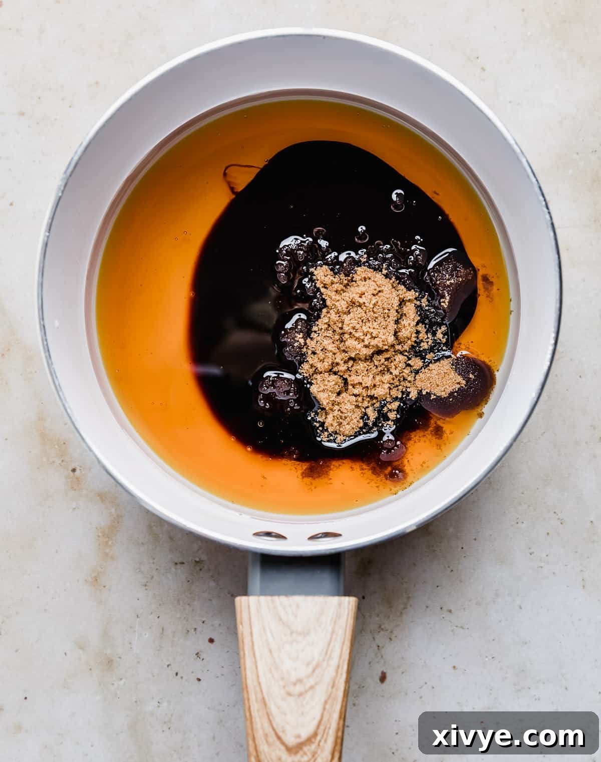 Festive Gingerbread Granola 6 A white saucepan on a stovetop with oil, honey, molasses, and brown sugar simmering together.