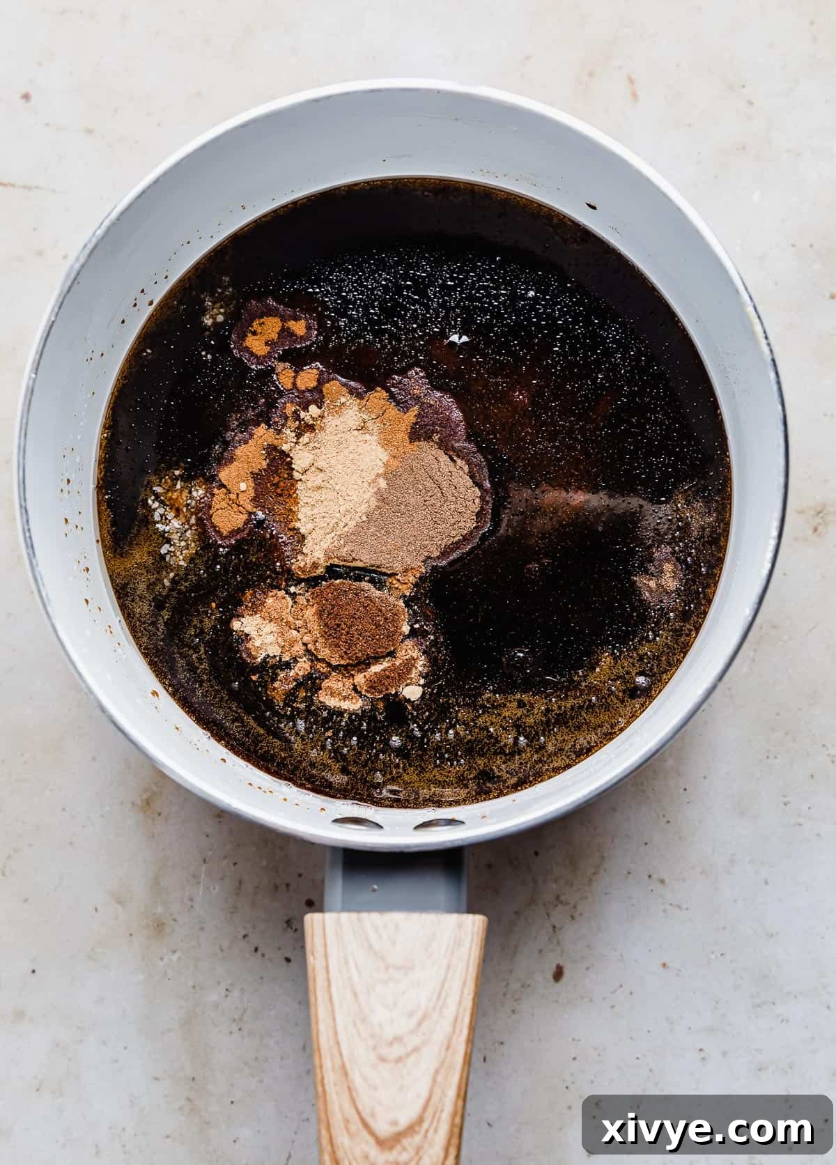 Festive Gingerbread Granola 7 The dark, glossy liquid mixture in a white saucepan, with ground gingerbread spices freshly stirred in, releasing a rich aroma.