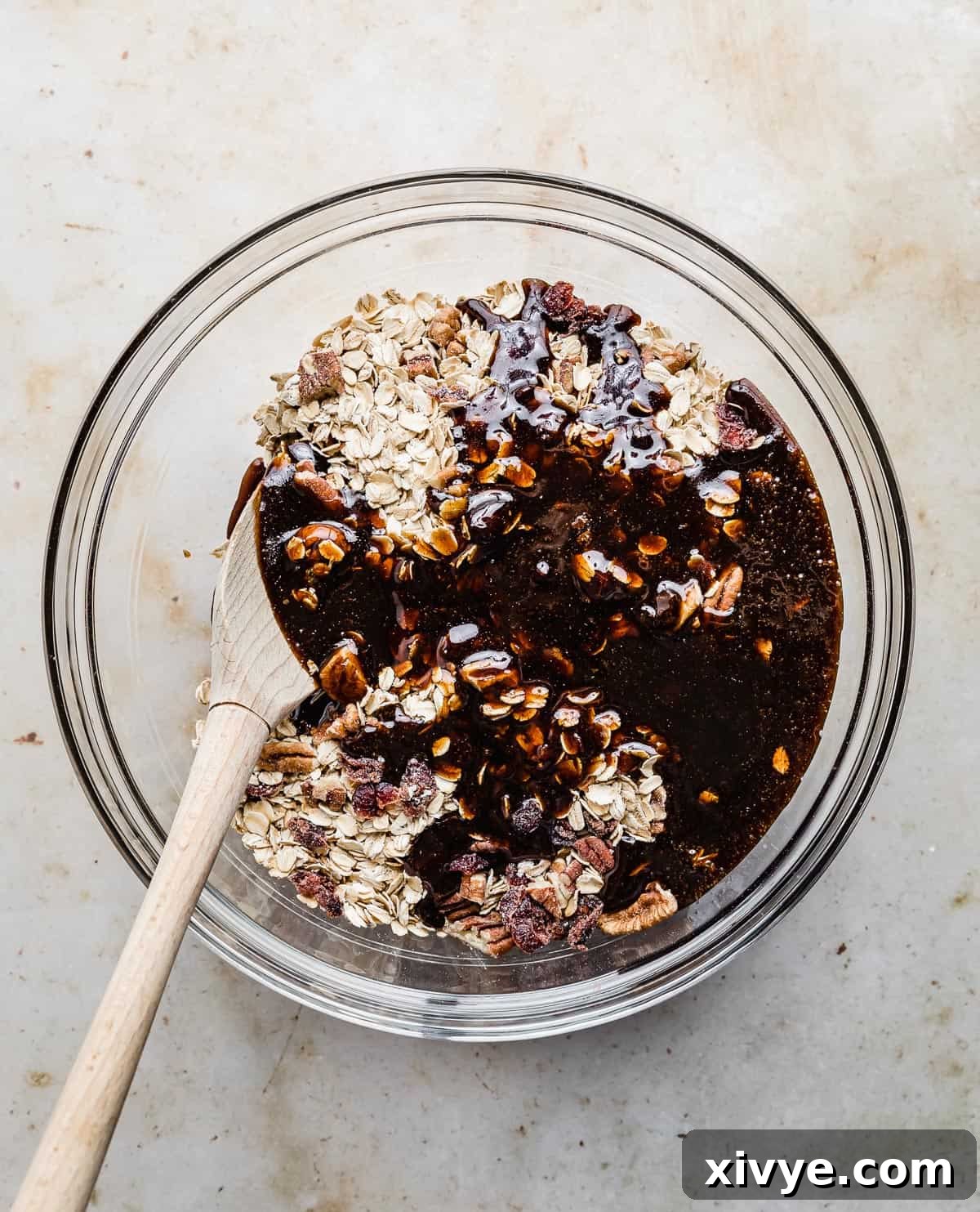 Festive Gingerbread Granola 8 The dark molasses and spice mixture being poured over the dry oat and pecan blend in a glass bowl.