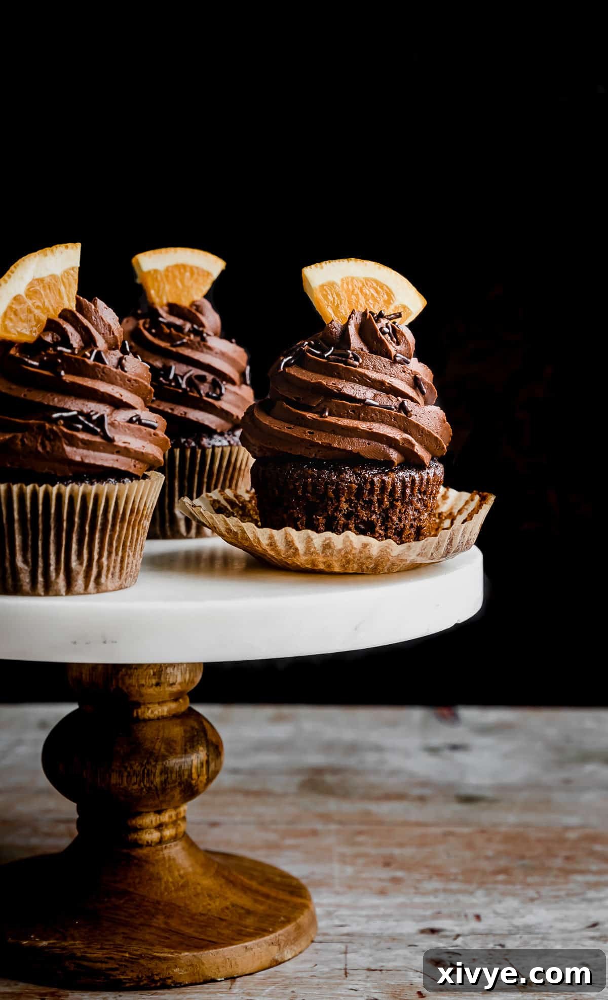 Chocolate Orange Cupcakes on a white marble topped cake stand against a black background.