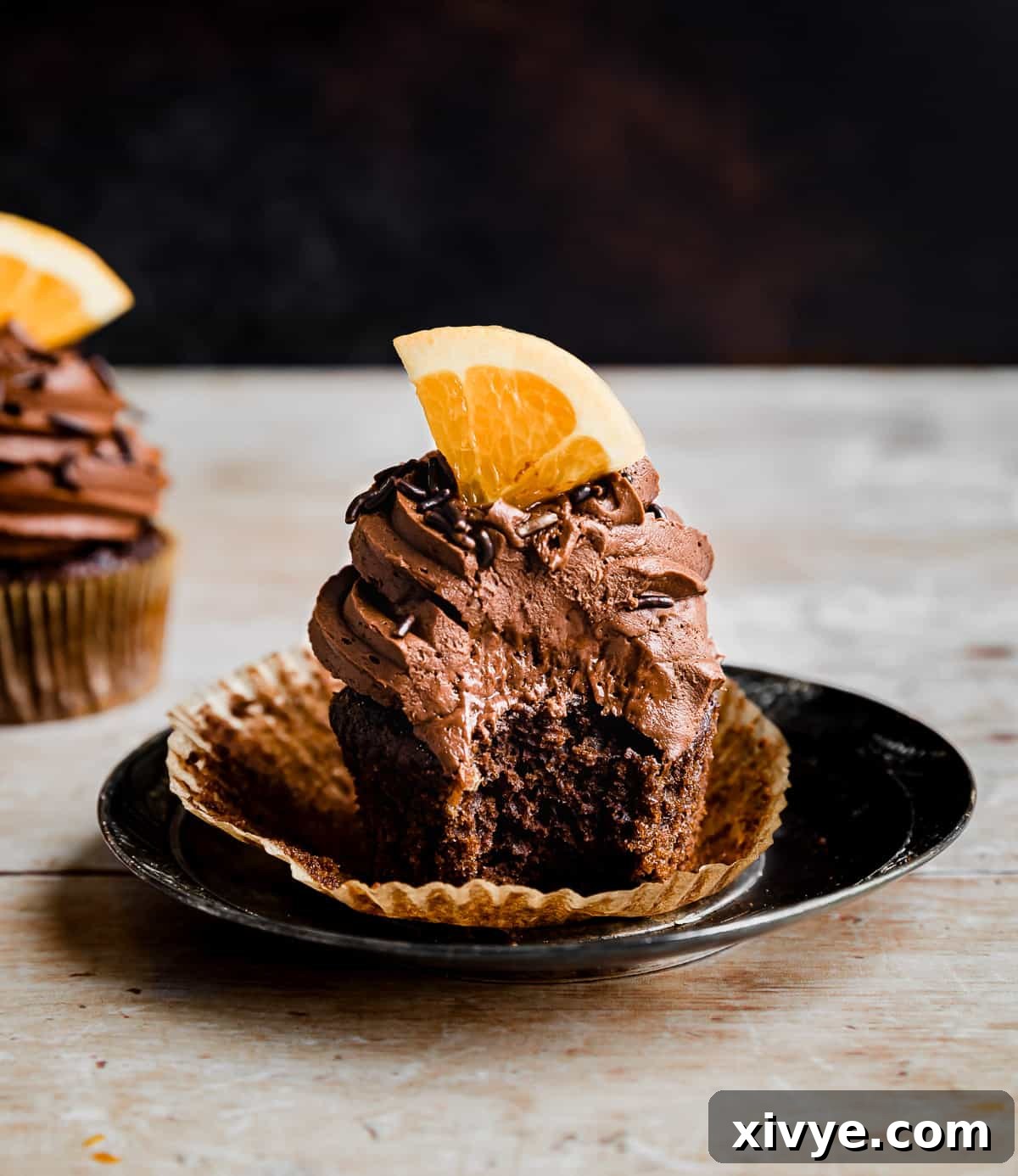 A bite taken out of a fresh orange topped chocolate orange cupcake.