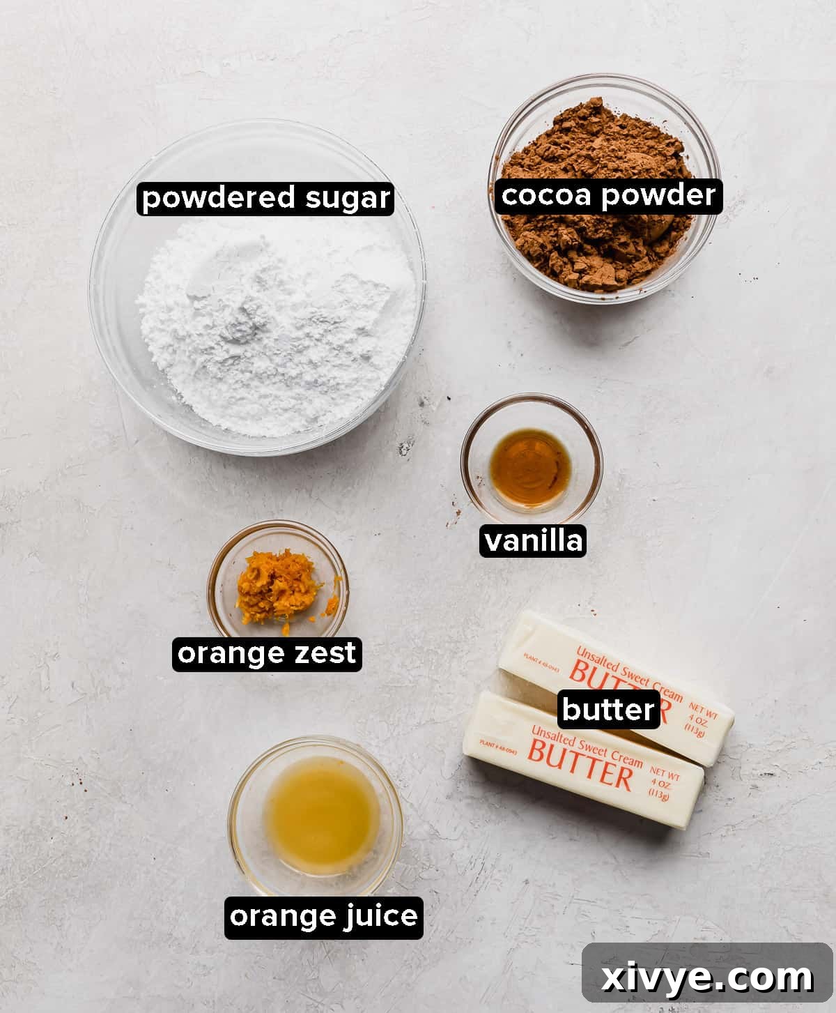 Chocolate Orange Frosting ingredients in glass bowls: butter, orange juice and zest, vanilla, cocoa powder, and powdered sugar.