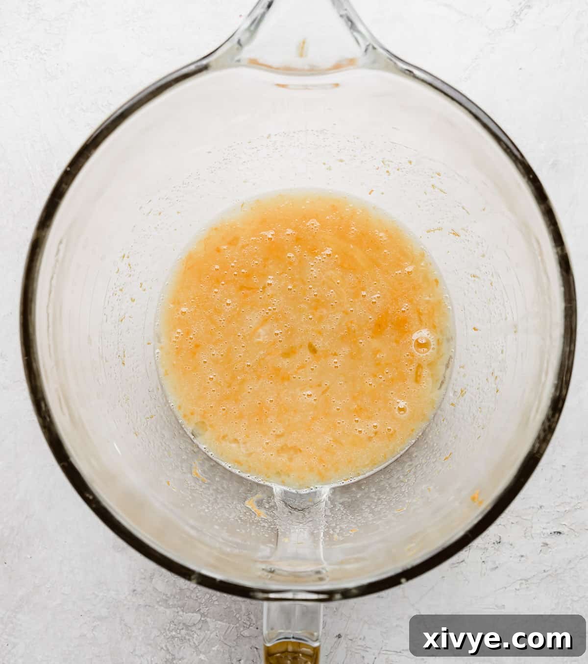 A glass stand mixer bowl with an orange liquid mixture in it.