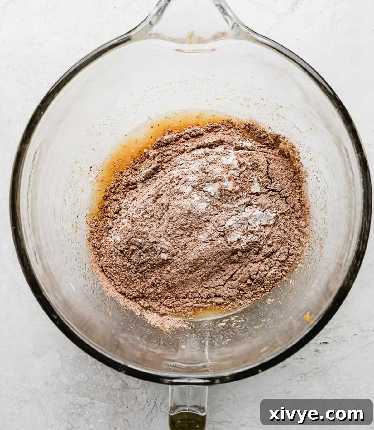 A light brown flour mixture in a glass stand mixer bowl on a gray background.