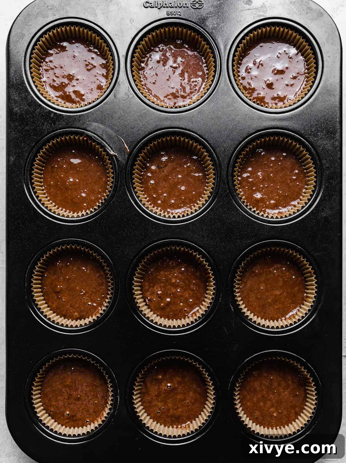 A twelve cupcake pan with tan cupcake liners filled with chocolate batter.