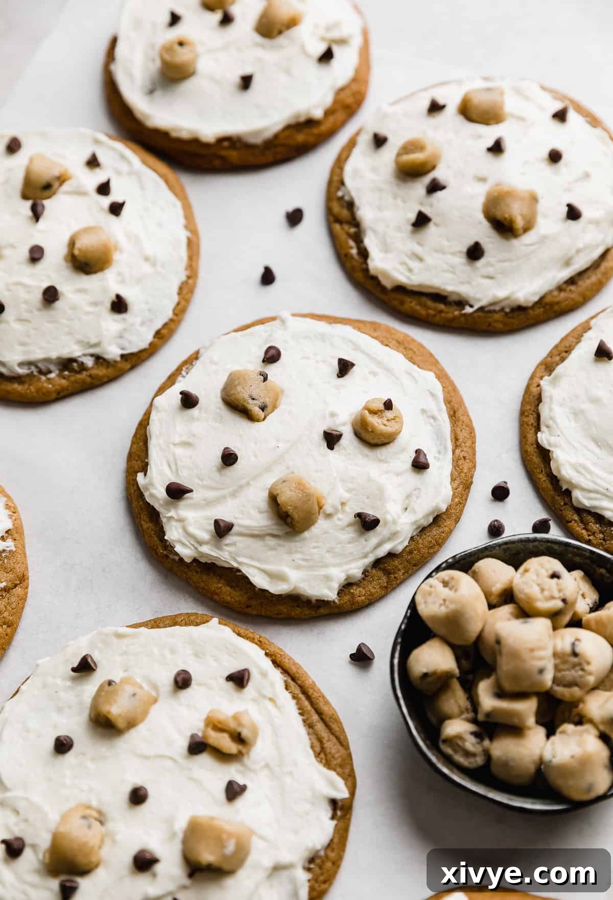 Crumbl Cookie Dough Dream 11 Crumbl Cookie Dough Cookies topped with white frosting, mini chocolate chips, and edible cookie dough chunks.