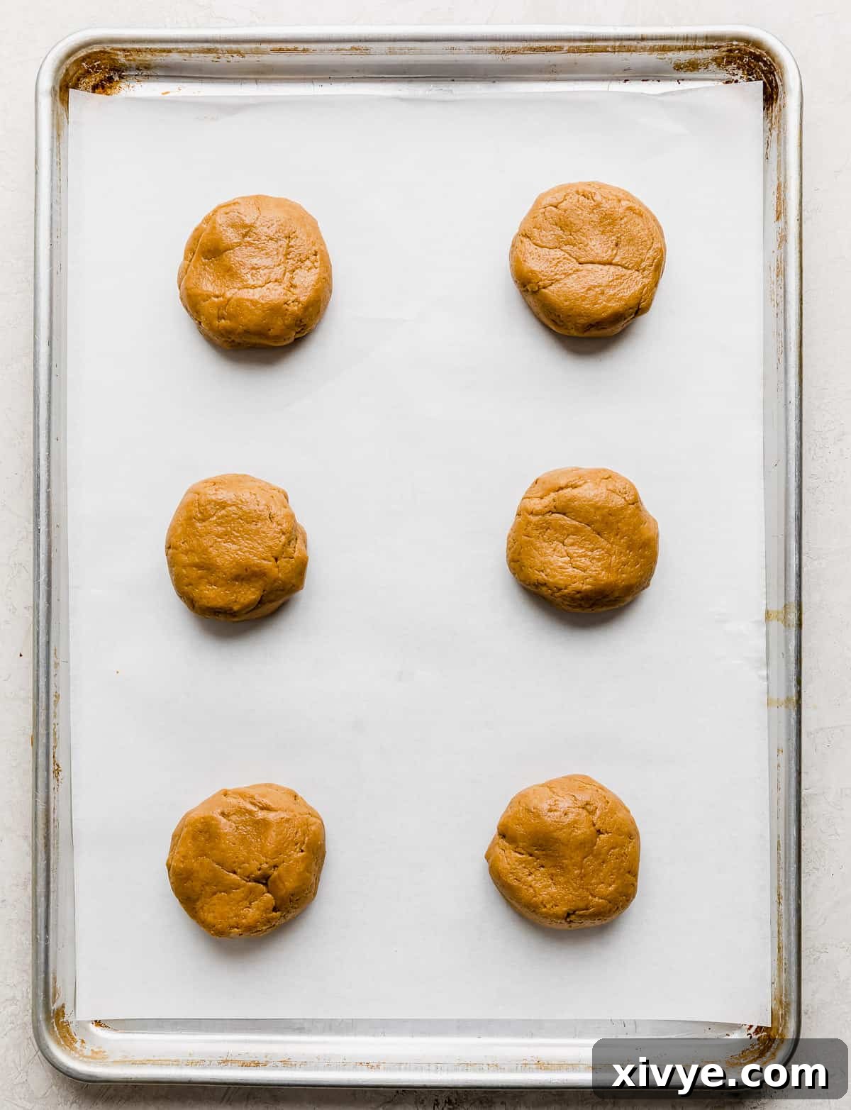 Crumbl Cookie Dough Dream 7 Six cookie dough cookie balls on a white parchment lined baking sheet.
