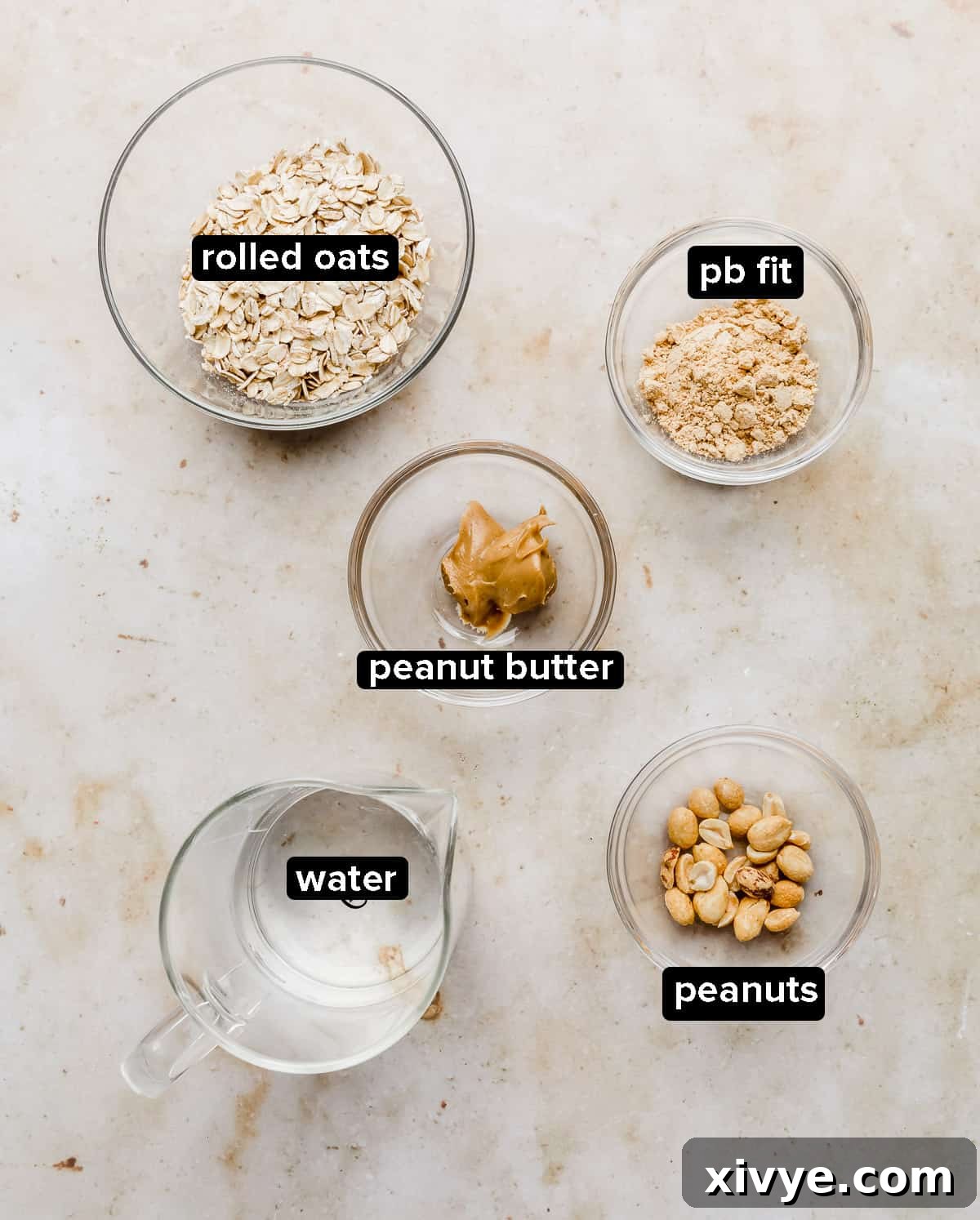Peanut Butter Oatmeal ingredients in glass bowls on a tan marble background.