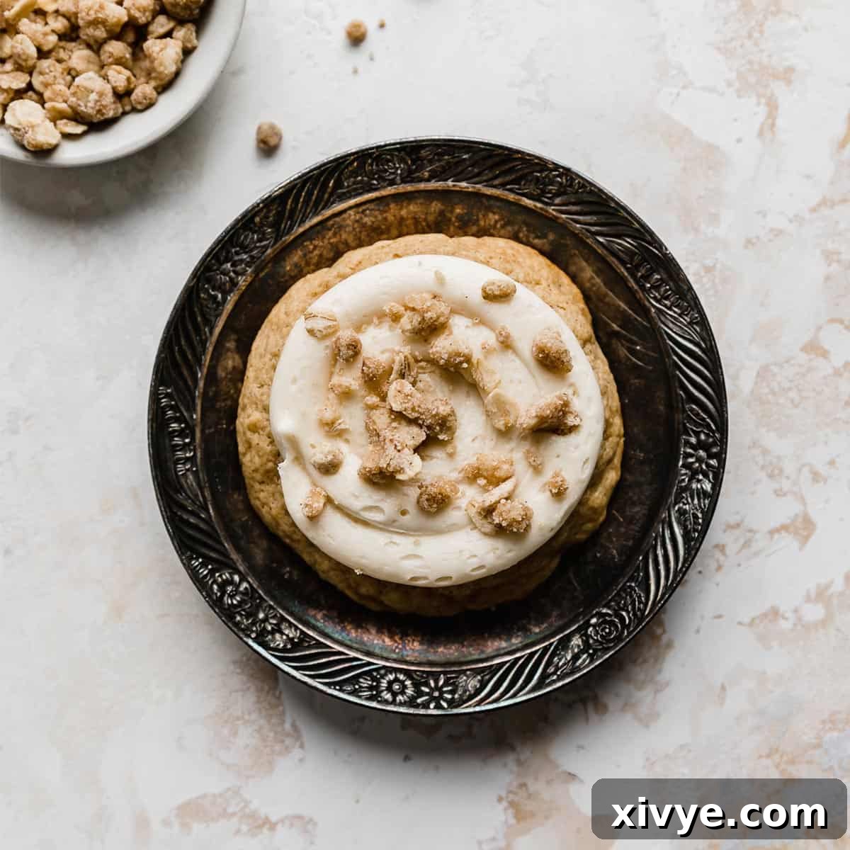 A beautifully crafted Caramel Apple Cookie, topped with creamy caramel frosting and a crumbly streusel, resting on a vintage black plate, evoking a cozy autumn feel.