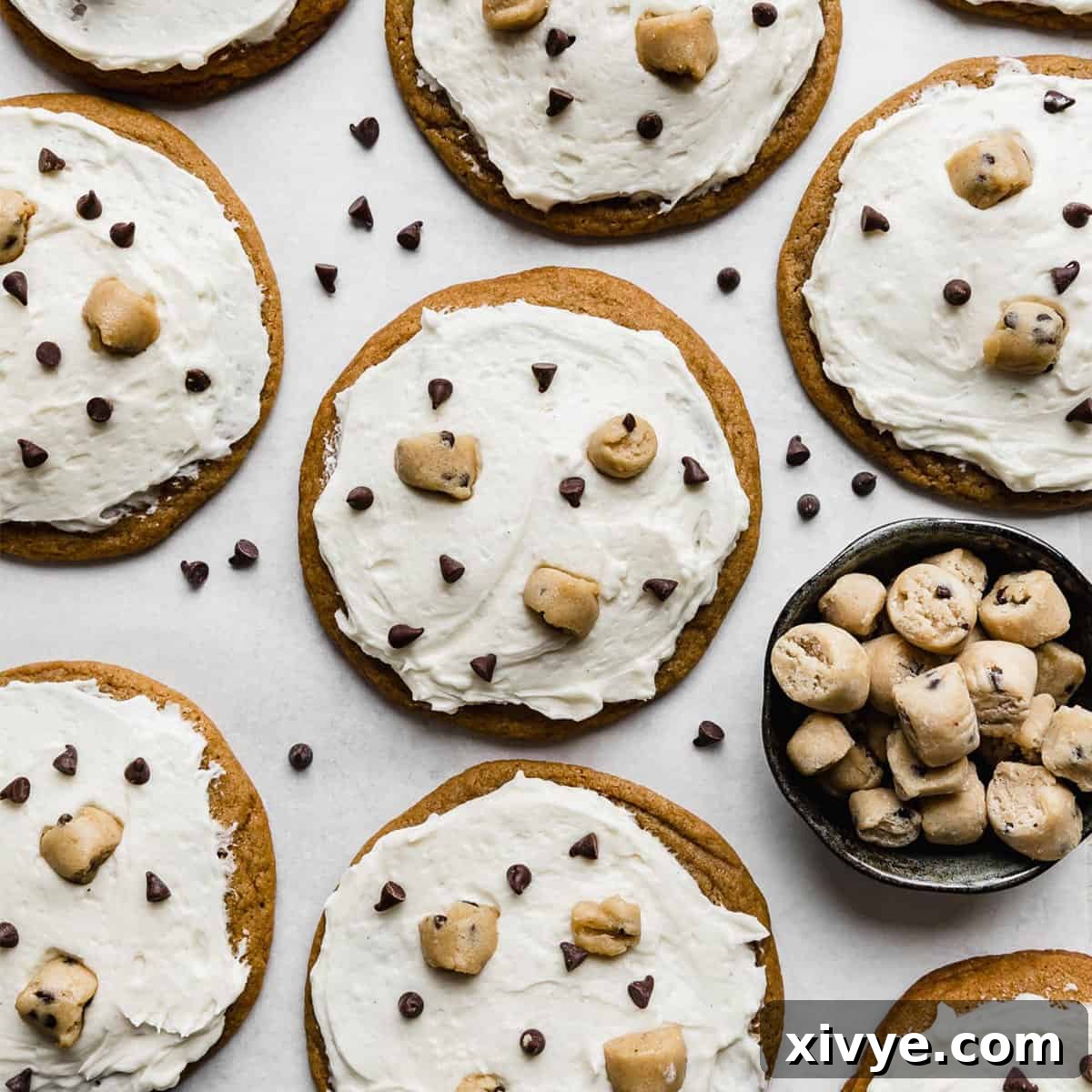 Crumbl Cookie Dough Cookies topped with white ice cream flavored frosting, mini chocolate chips, and edible cookie dough bites.