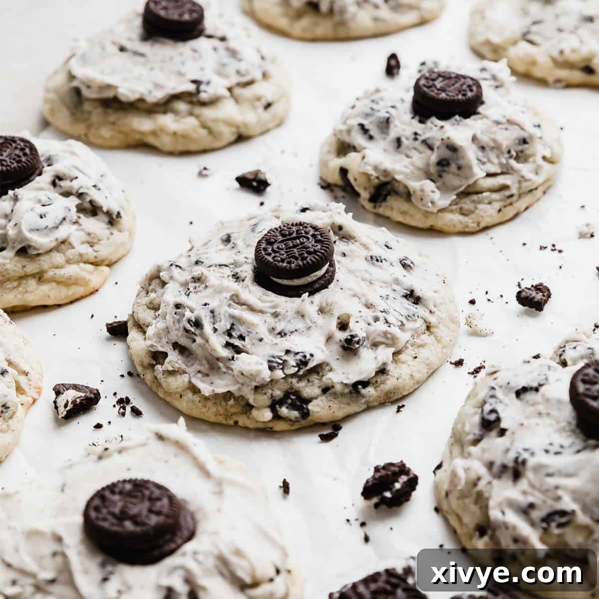 A sumptuous Crumbl Cookies and Cream Milkshake Cookie, featuring an Oreo cookie base, lavishly frosted with cookies and cream icing, and garnished with a mini Oreo, presented on white parchment paper.
