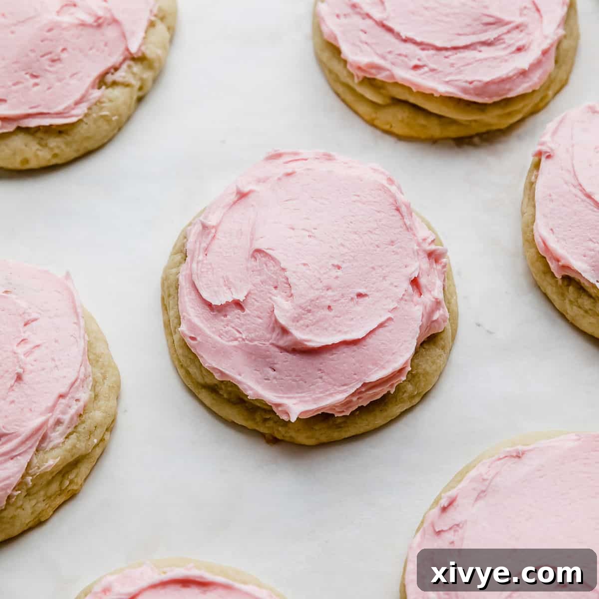 A beautifully frosted copycat Crumbl sugar cookie with distinctive pink almond frosting, set against a clean white background.