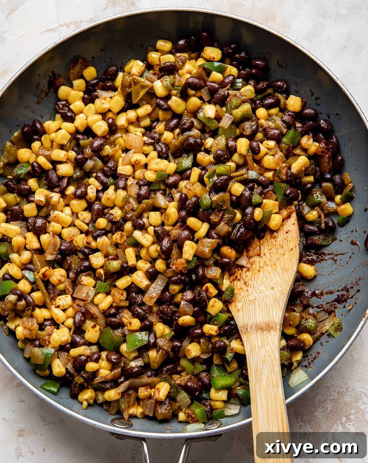 A close-up view of the savory corn, black bean, and pepper mixture simmering gently in a gray skillet, heated through and ready to be used as a quesadilla filling.