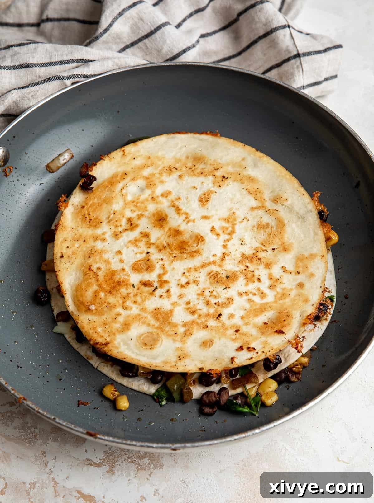 A perfectly cooked Black Bean and Corn Quesadilla, golden brown and crispy, sizzling in a gray skillet, indicating it is ready to be flipped to cook the second side.