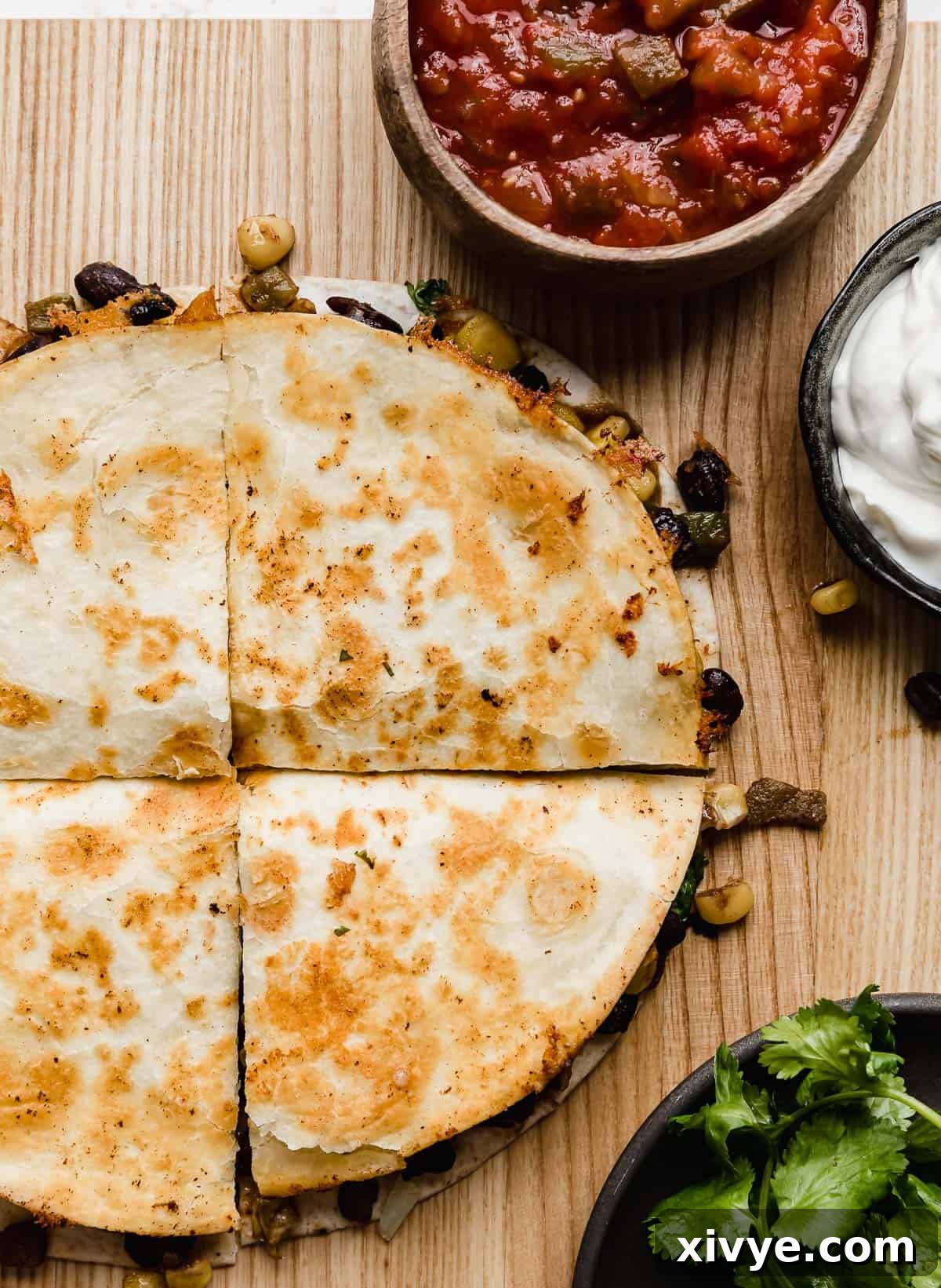 Close up photo of a Black Bean and Corn Quesadillas cut into perfect wedges on a rustic brown cutting board, garnished with fresh cilantro and ready for serving.