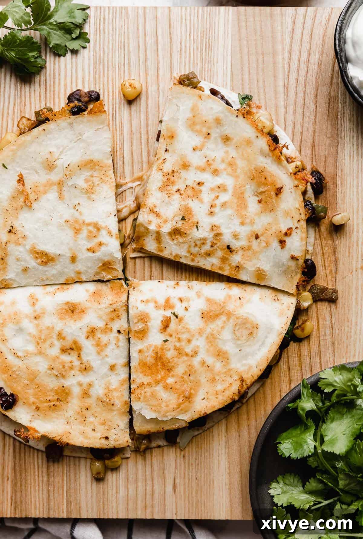 A whole Black Bean and Corn Quesadilla, beautifully presented on a rustic brown board, surrounded by fresh cilantro, awaiting to be sliced and served.