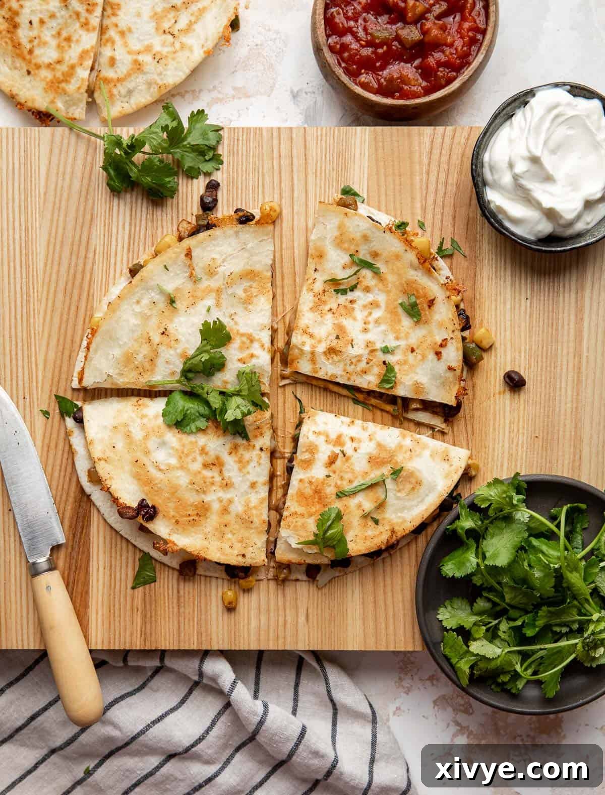 A beautifully arranged spread of Black Bean and Corn Quesadilla wedges on a wooden cutting board, surrounded by fresh sour cream, vibrant cilantro, and rich salsa, ready for a gathering.