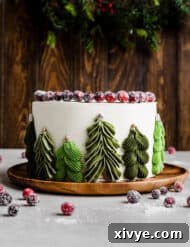 A white chocolate orange cranberry cake with green Christmas trees piped along the side of the cake, a delicious holiday treat.