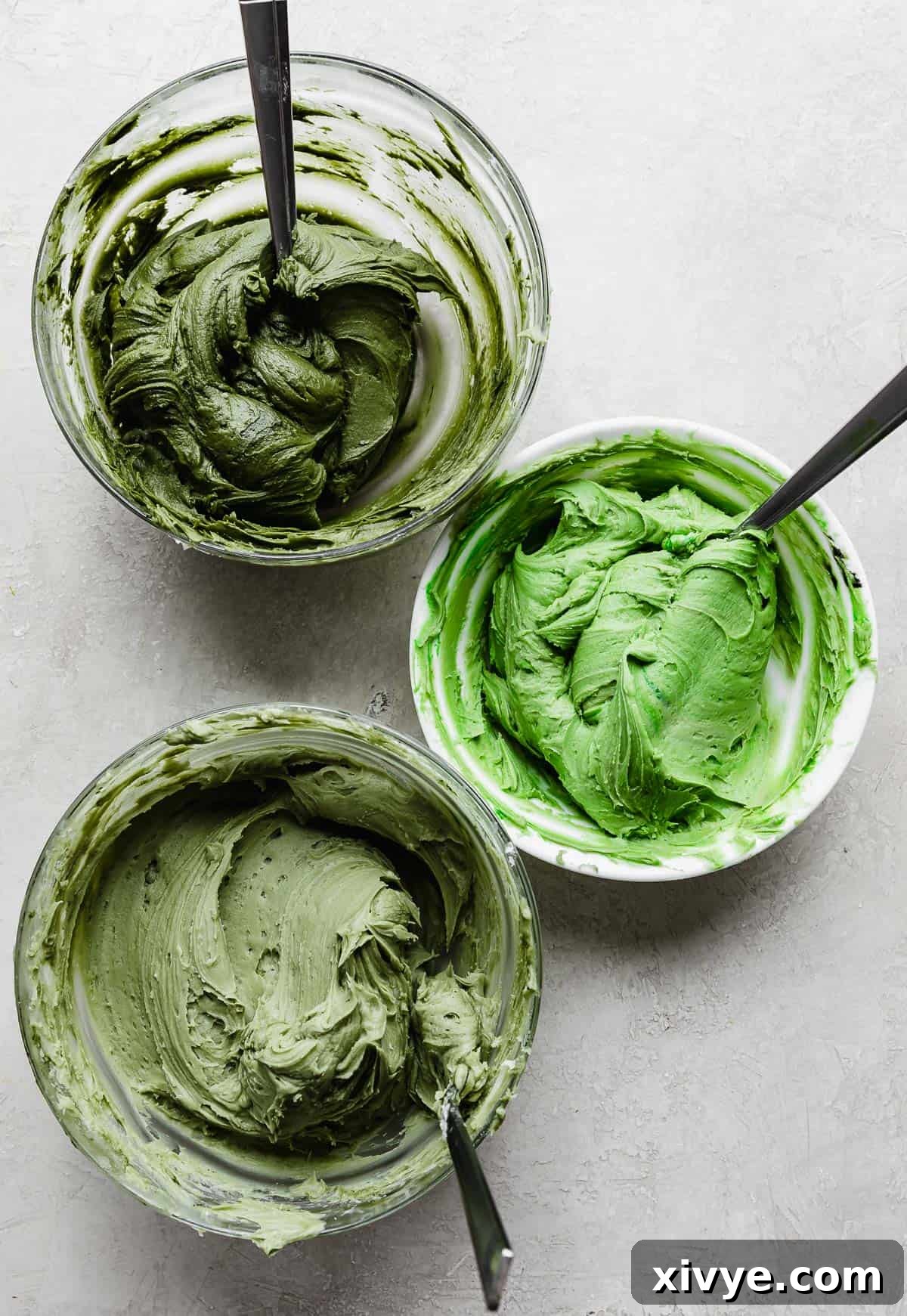 Three bowls of differing shades of green buttercream, for making festive Christmas trees on a Christmas Tree Cake.