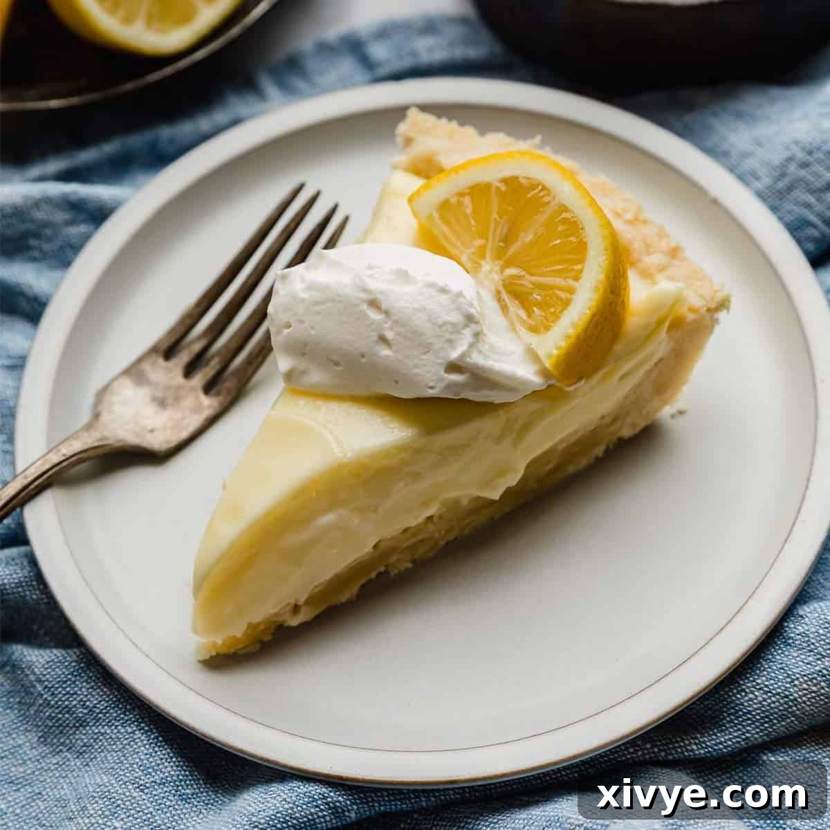 Lemon Sour Cream Pie on a white plate with a dollop of whipped cream and lemon slice on top.