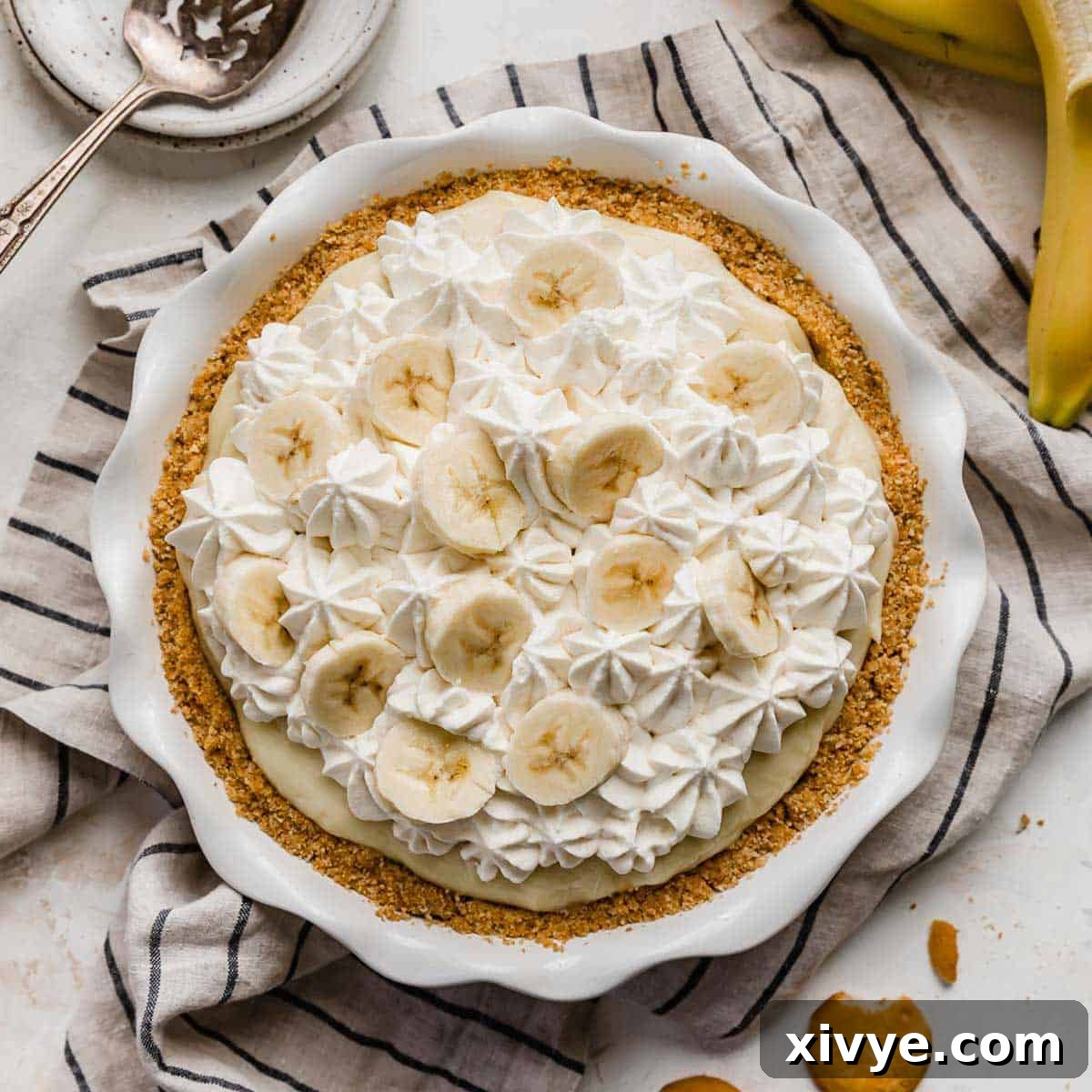 An old fashioned banana cream pie with homemade custard, topped with banana slices and whipped cream, on a linen striped napkin.