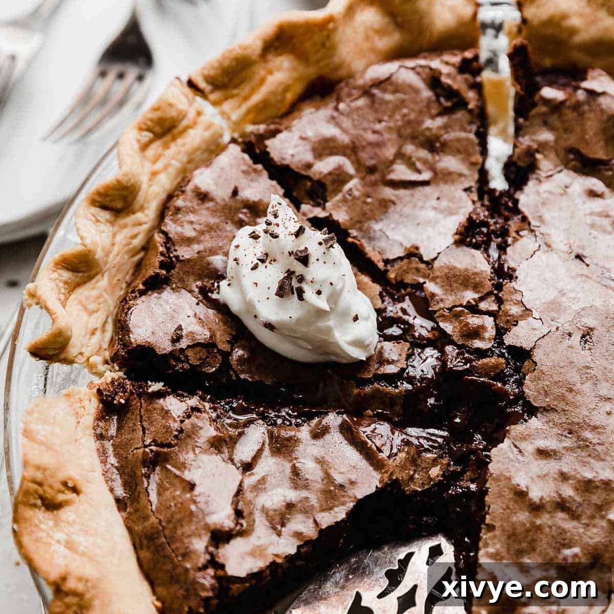 A brownie pie sliced into several servings, with one slice topped with white whipped cream and chocolate shavings.