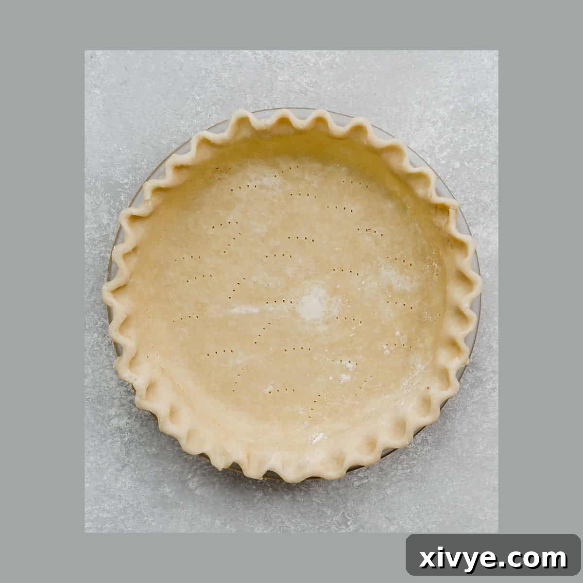An All Butter Food Processor Pie Crust in a pie plate with fluted edges on a gray background.