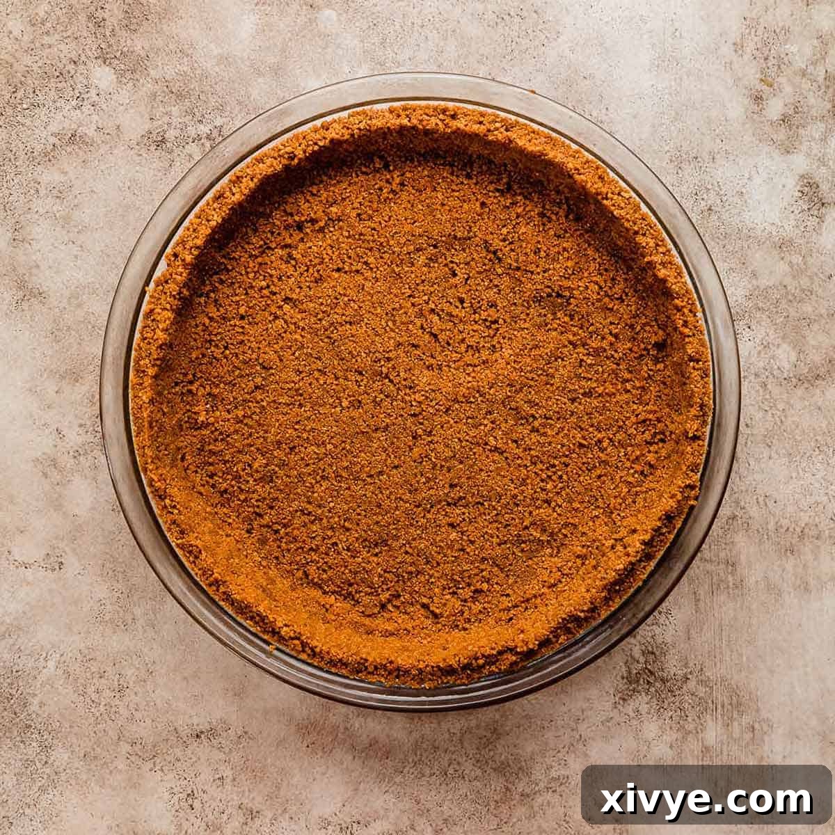 A deep orange colored Biscoff Pie Crust on a beige textured background.