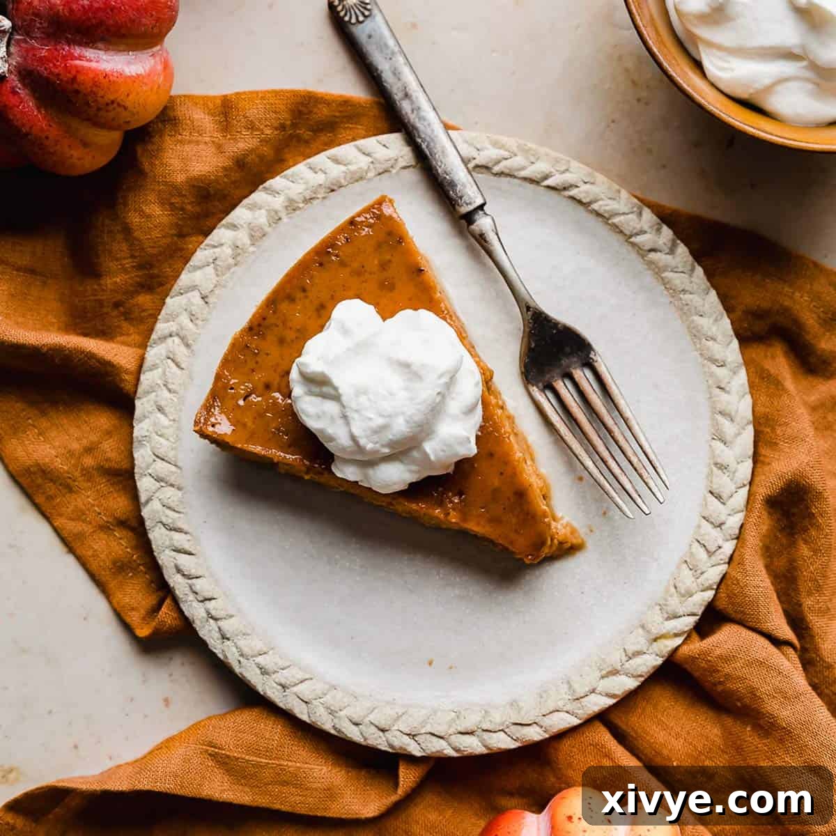 Overhead photo of a slice of whipped cream topped Crustless Pumpkin Pie on a plate with a fork to the side.