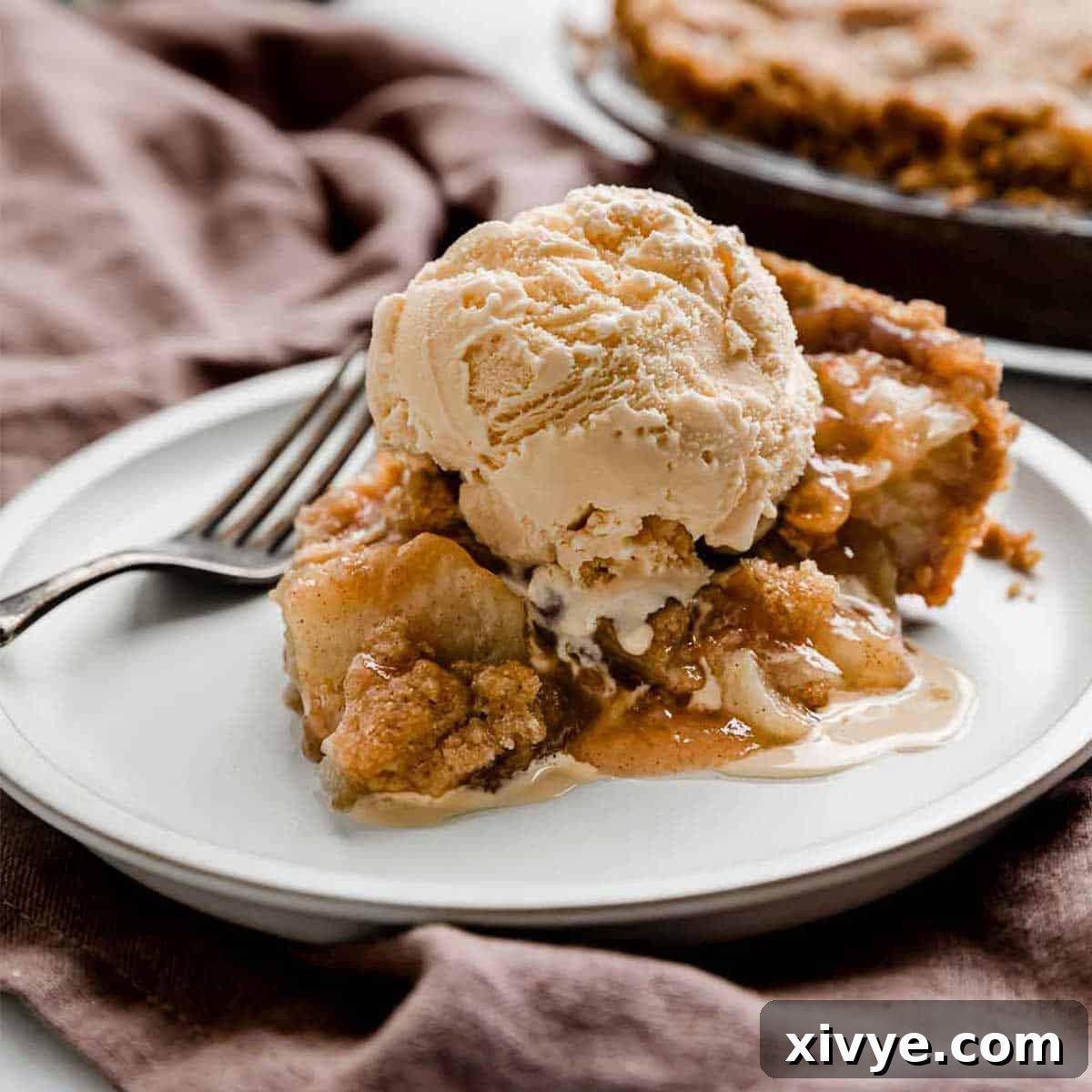 An Apple Pie slice on a white plate topped with a scoop of vanilla ice cream.