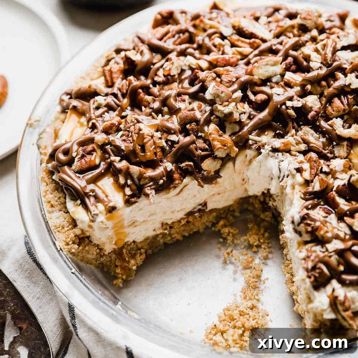 A turtle pie with a pecan crust, caramel cream cheese filling, and chocolate caramel pecan topping.