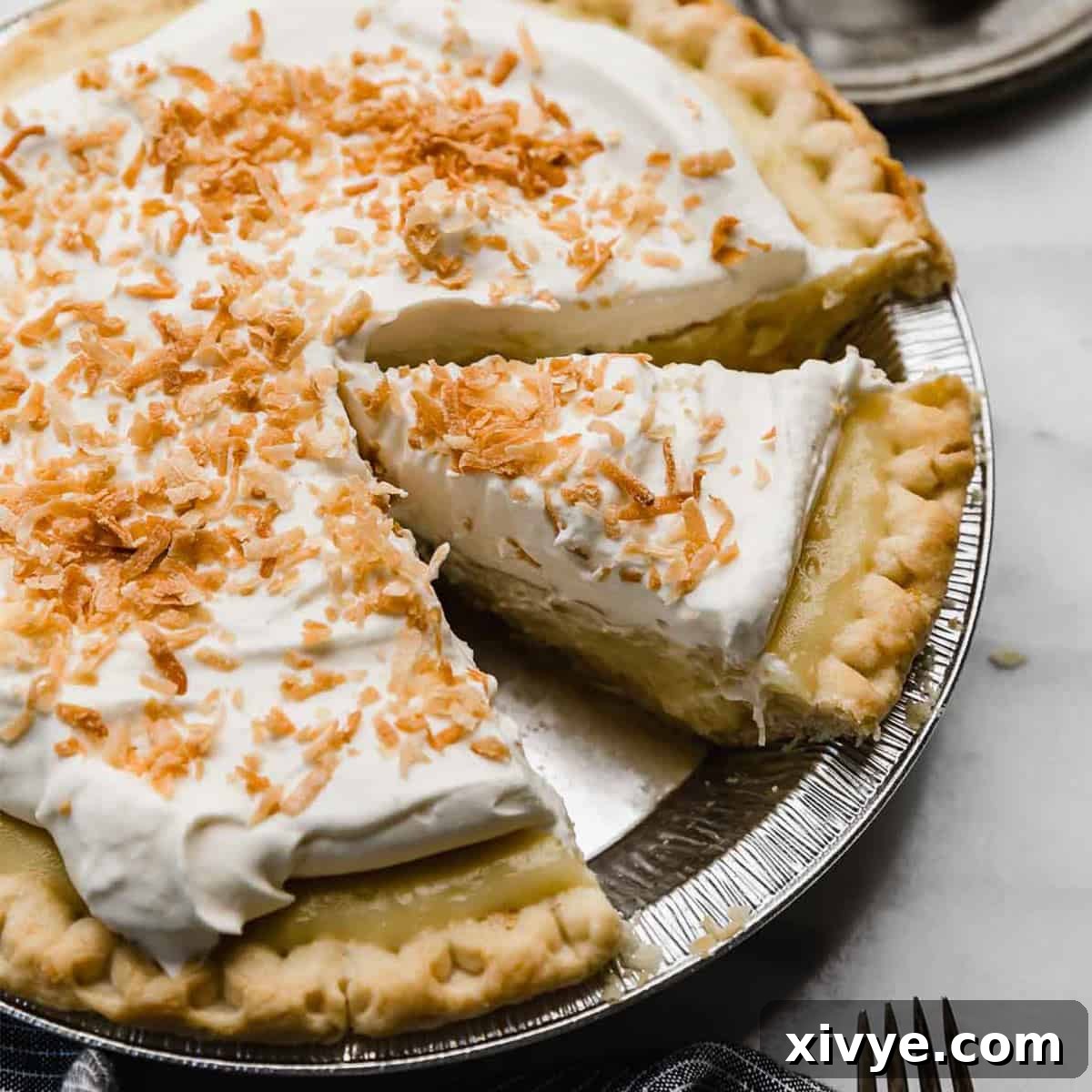 A slice of coconut cream pie, topped with toasted coconut in a pie plate.