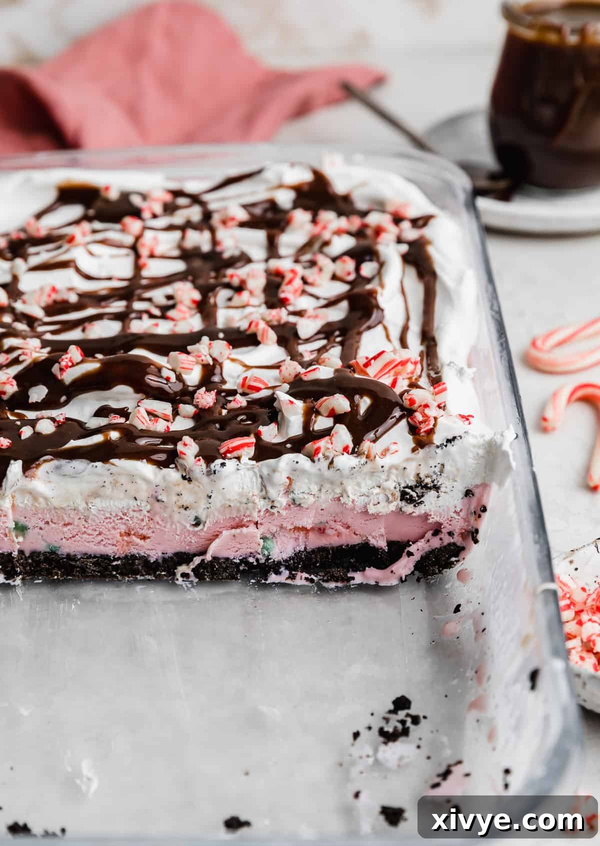 A close-up view of a large slice of Christmas Ice Cream Cake, clearly showing the distinct layers: dark Oreo crust, light pink peppermint ice cream, creamy white whipped topping, and a sprinkle of crushed candy canes on top.