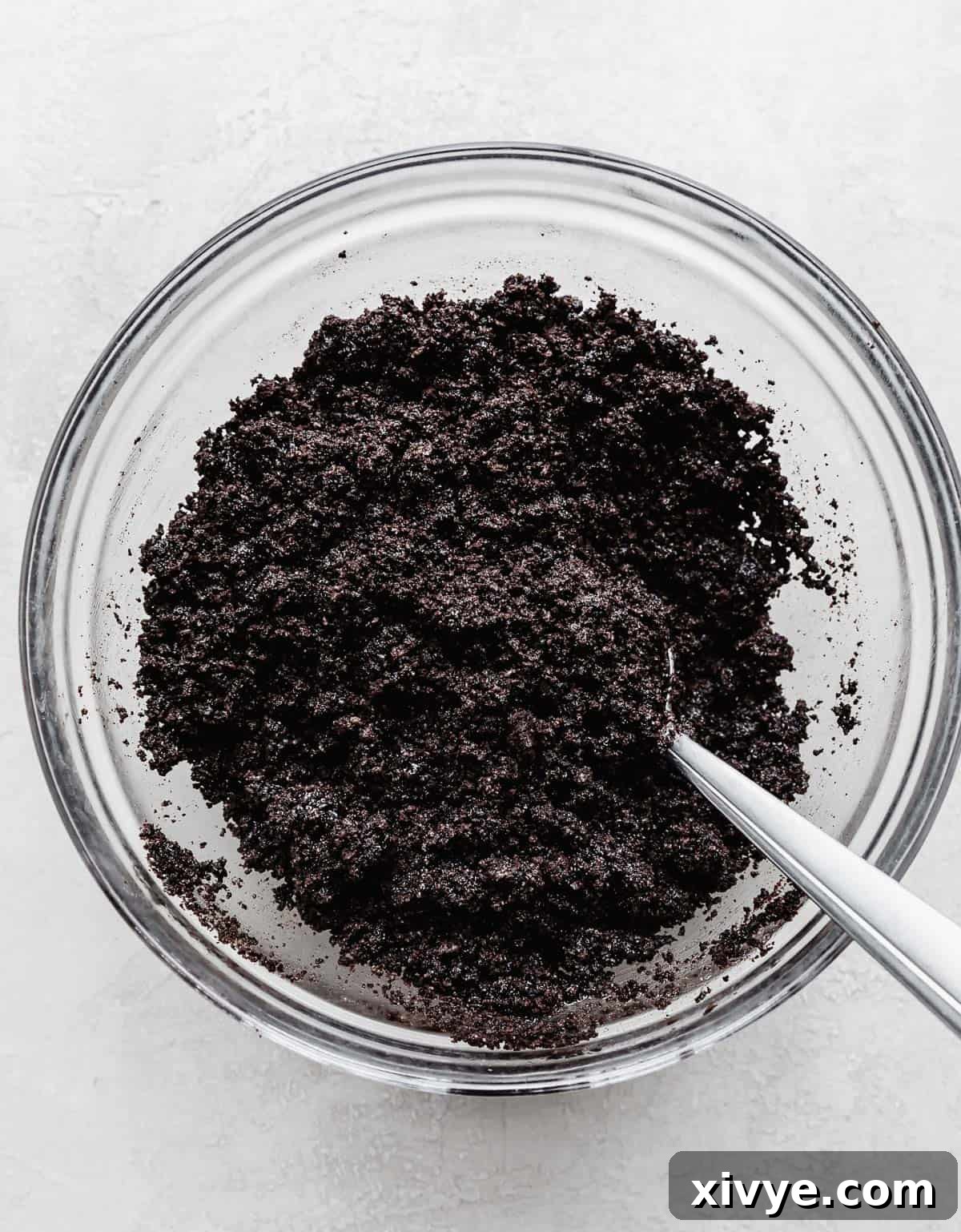 A glass bowl filled with finely crushed Oreo cookie crumbs, ready to be mixed with butter for the crust.