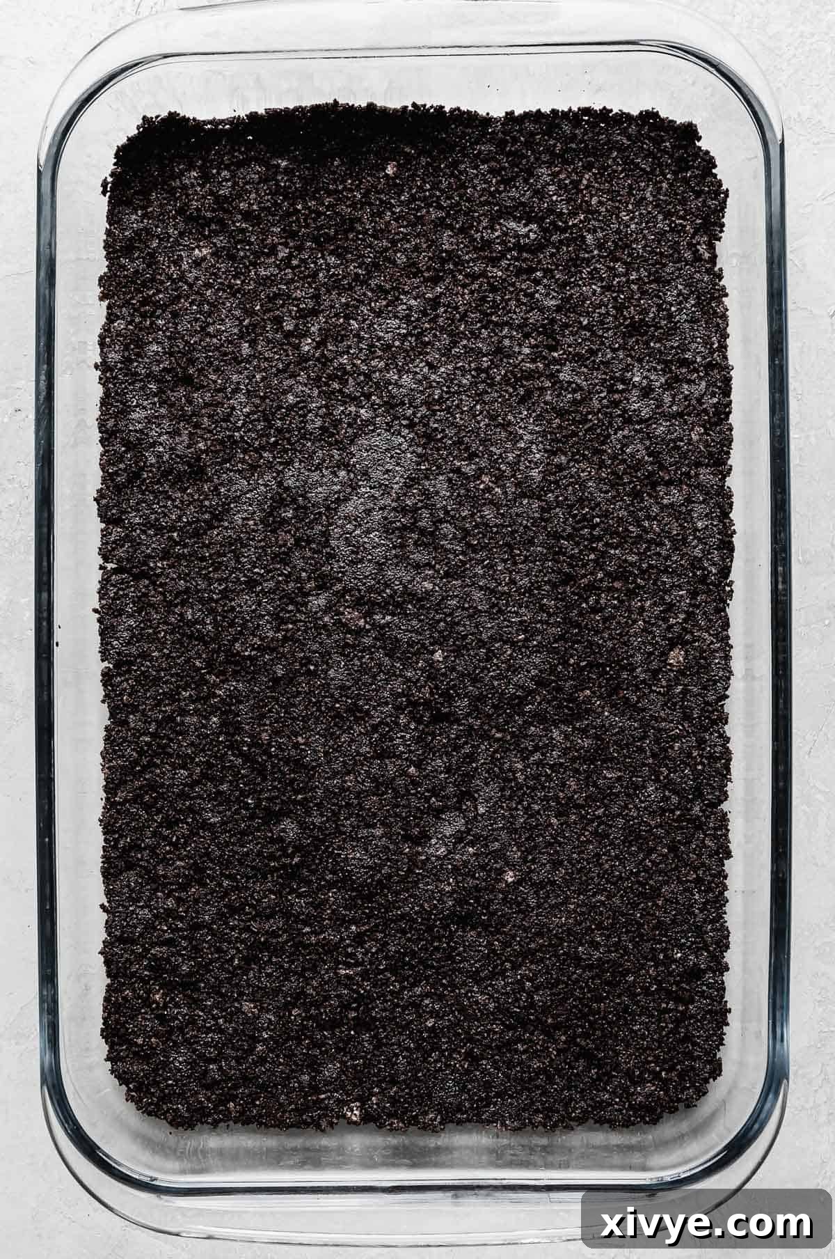 A rectangular glass baking dish with the compacted Oreo crust evenly pressed along the bottom, ready for the next layer.