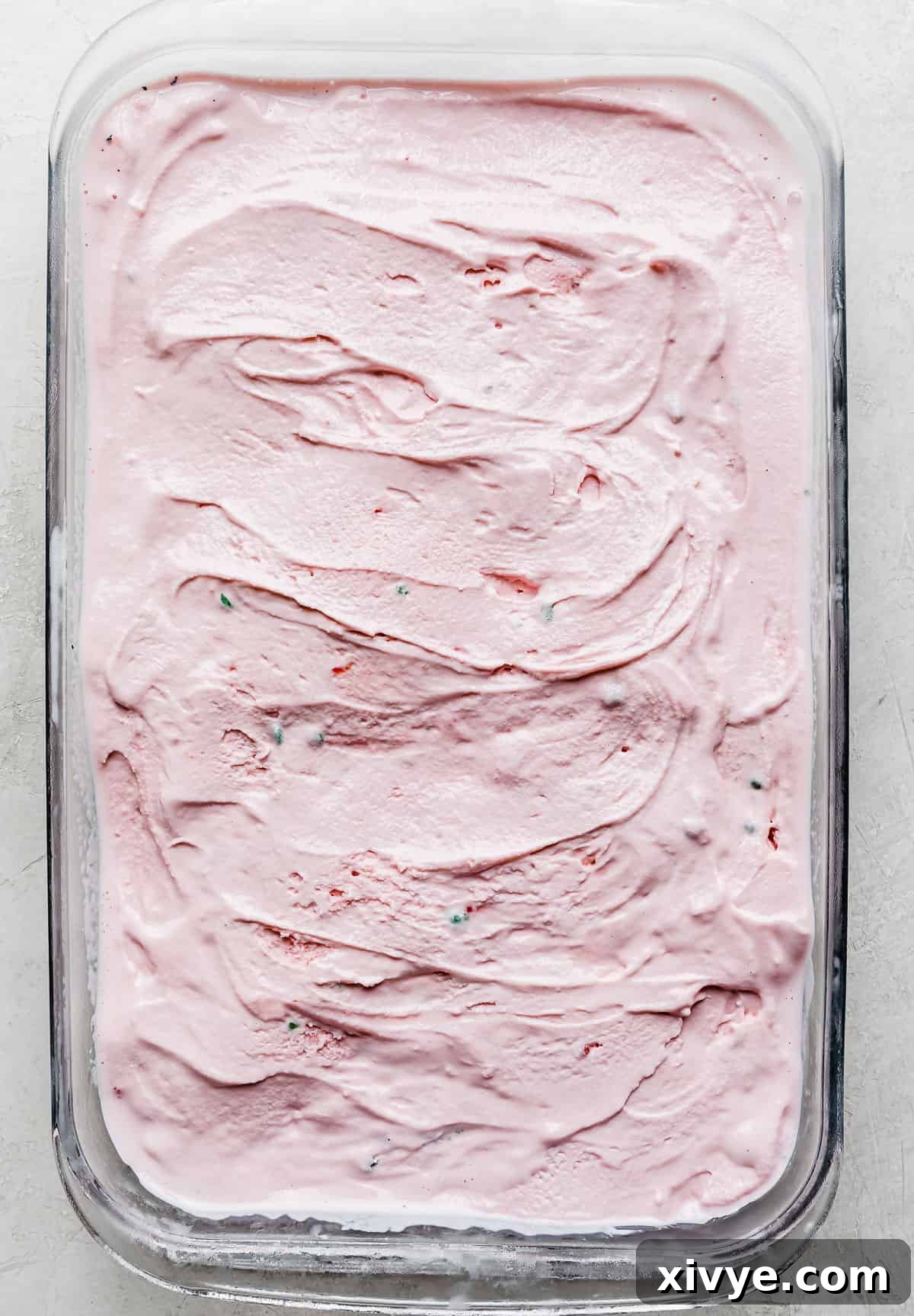 A rectangular glass dish filled with a smooth, even layer of pink peppermint ice cream over the dark Oreo crust.
