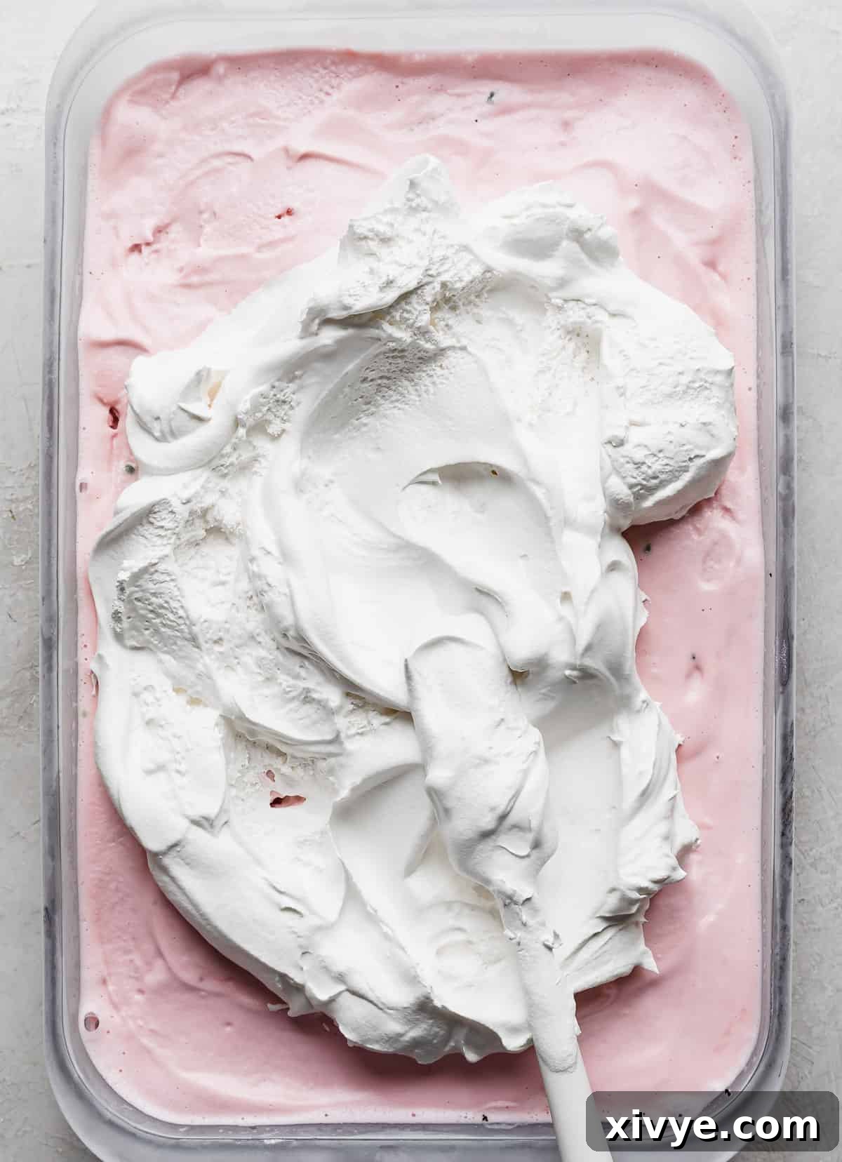 White Cool Whip being carefully dolloped onto the center of the firm peppermint ice cream layer in a rectangular dish.
