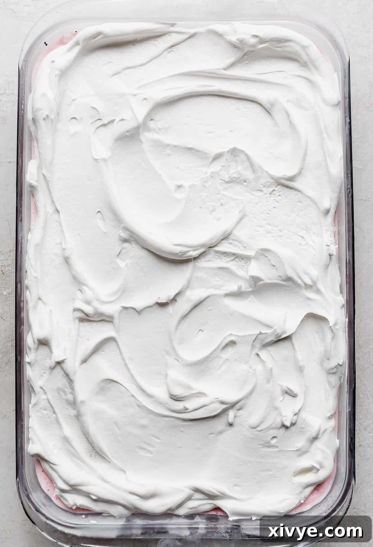 A finished glass baking dish of peppermint Christmas ice cream cake topped with a generous layer of white whipped cream.