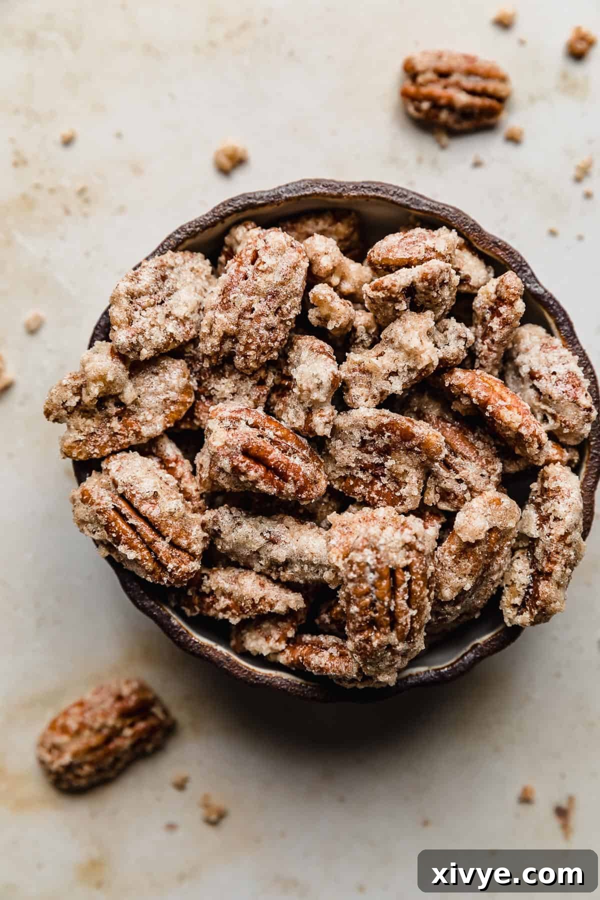 Sweet Glazed Pecans 2 A black bowl brimming with perfectly roasted candied pecans, set against a warm tan marble background.