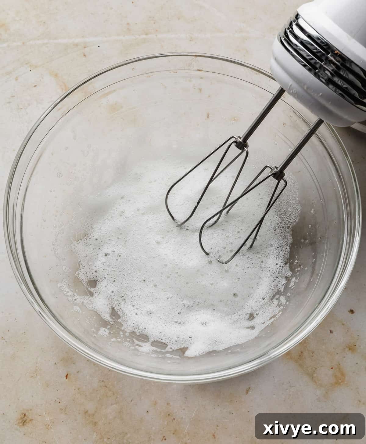 Sweet Glazed Pecans 5 A hand mixer expertly whipping egg whites until they reach a frothy consistency in a clear glass bowl, showing the texture change.
