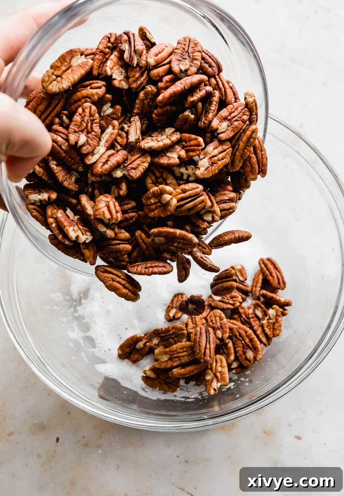 Sweet Glazed Pecans 6 Raw pecan halves being gently poured into a glass bowl, ready for the next step in the recipe preparation.