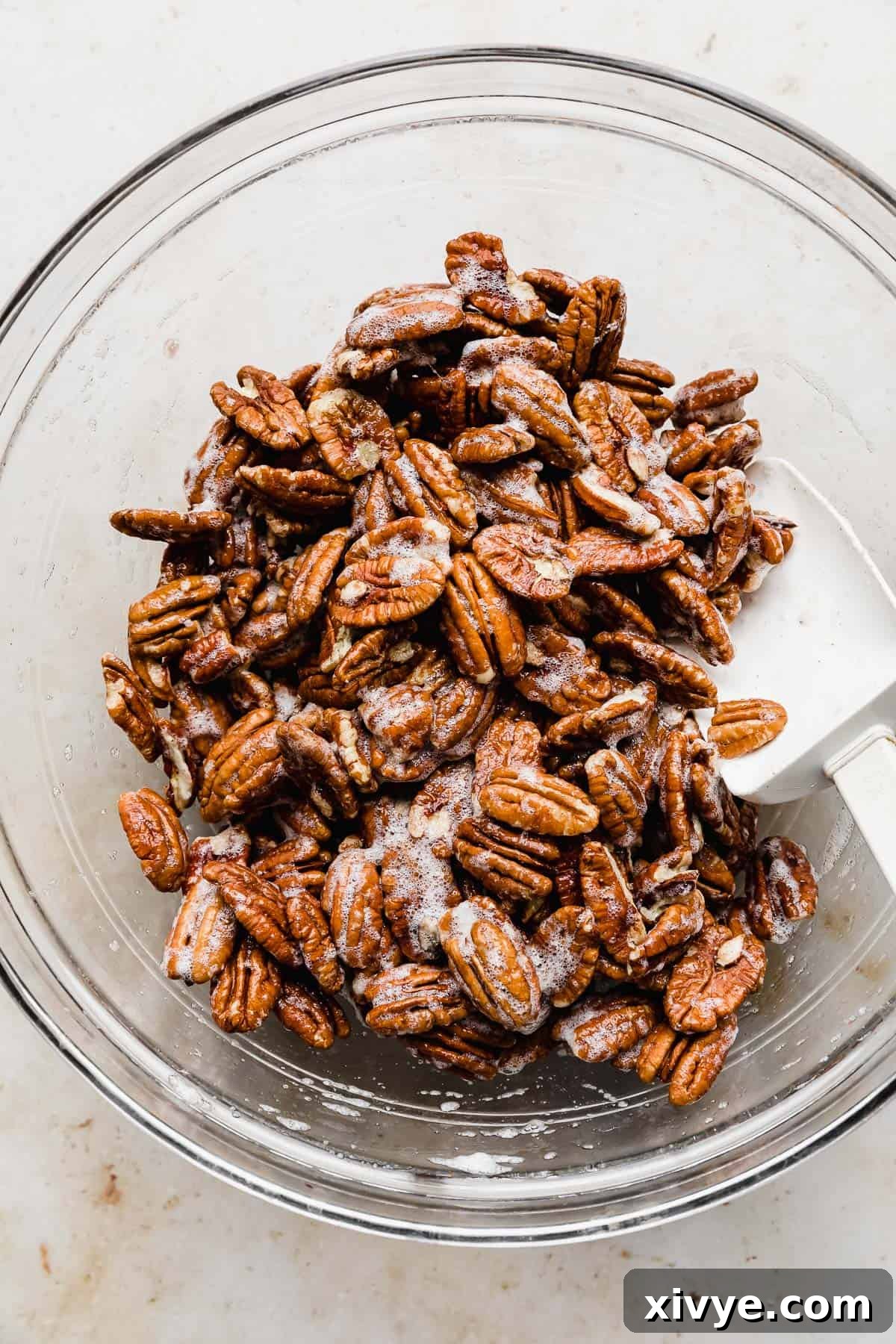Sweet Glazed Pecans 7 Raw pecans being gently mixed in frothy egg whites within a glass bowl, illustrating the coating process.