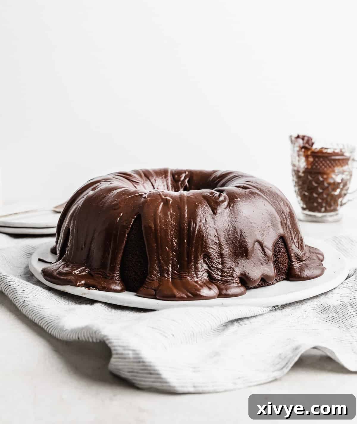 A chocolate frosting covered chocolate Bundt Cake on a white plate against a white background.
