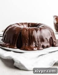 A chocolate frosting covered Chocolate Buttermilk Bundt Cake on a white plate against a white background.