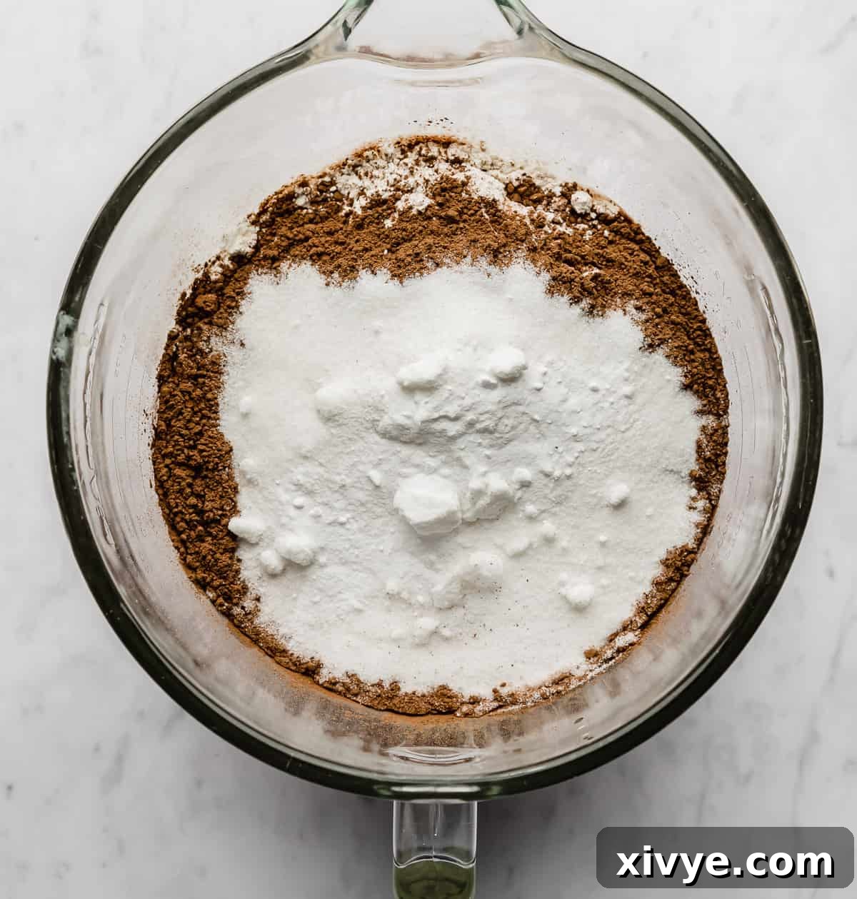 A glass mixing bowl with cocoa, sugar, and flour in it.